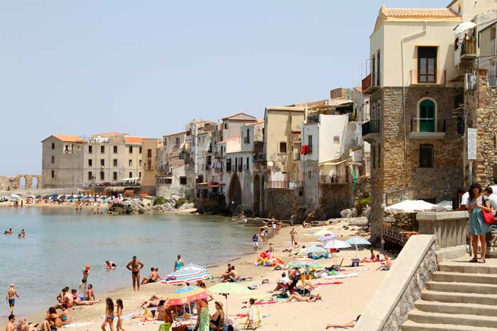 The Norman cathedral of Cefalù rising above the medieval rooftops with La Rocca behind and the Tyrrhenian Sea in the foreground
